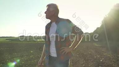 快乐的老农夫穿着衬衫站着，用愉快的表情看着他的田野，美丽的自然景观。